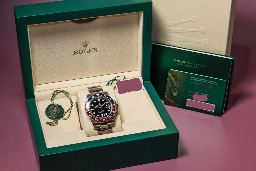 Rolex watch in open green box with accessories on a pink background